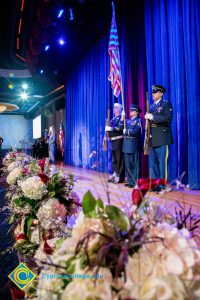 Military Color Guard on stage with white flowers along the bottom of the stage.