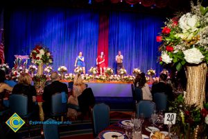 Young women and a young man on stage with white flowers along the bottom of the stage.