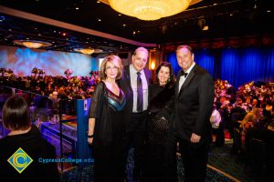 Woman with short blond hair in a blue and black dress, a man in a suit and tie a woman with dark brown hair, wearing black, and a man in a black suit and bowtie.