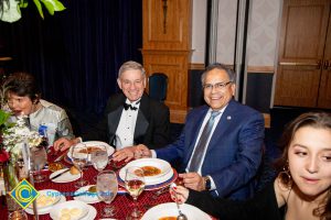 A woman eating, two men in suits smiling and a woman looking to the side.