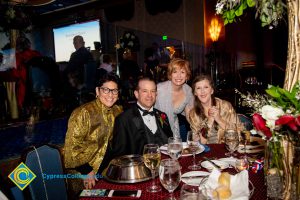 Carmen Dominguez, Howard Kummerman, JoAnna Schilling and a woman with long brown hair and a gold wrap smiling at a dinner table.