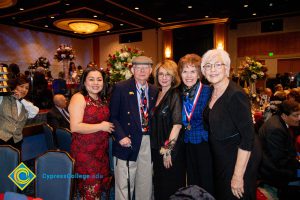 Four women smiling with a man wearing a hat and holding a cane.