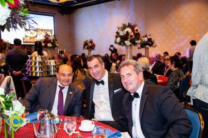 Three men in suits and tie smiling at the dining table.