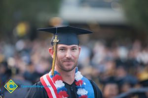 A smiling graduate with a red, white and blue lei around his neck.