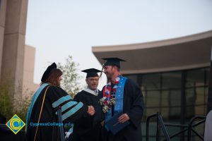 A graduate being congratulated while getting his degree on stage during commencement.