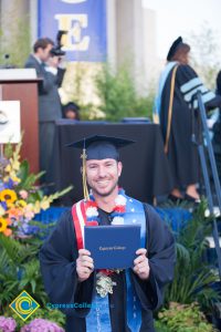 A smiling graduate holding his degree.