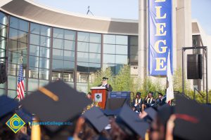 A sea of graduation caps with a graduate speaking on stage in the distance.