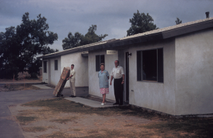 Man and woman standing outside original homes that were located across from the college and used as administrative offices and bookstore when the college opened.