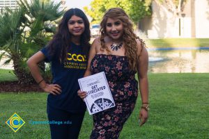 Female student wearing Cypress Collee Associated Students shirt next to another female student wearing a floral dress and necklace, holding a pamphlet