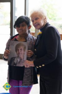 Holocaust survivor standing next to young girl, who is holding signed Yom HaShoah program