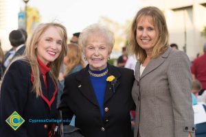 Holocaust survivor wearing black blazer and blue sweater, standing with woman wearing black and red blazer with red sweater and woman wearing tweed blazer and white top