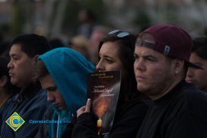 Three men and one woman watching Yom HaShoah event. Woman has the program over her mouth