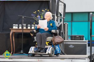 Holocaust Survivor Gerda Seifer sitting in wheelchair on stage giving speech
