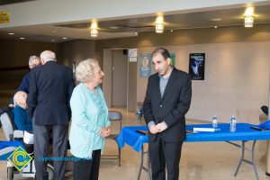 David Halahmy wearing a suit, speaking with Holocaust survivor who is wearing mint top and sweater and black pants