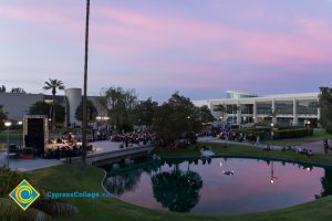 Campus at sunset, with pond seen in foreground, audience, stage, and library in background