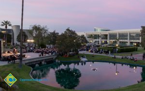 Campus at sunset, with pond seen in foreground, audience, stage, and library in background