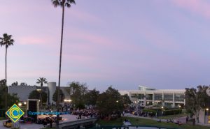 Campus at sunset, with pond seen in foreground, audience, stage, and library in background