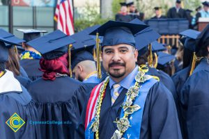 A student poses in graduation regalia, a Veteran's Resource Center sash and a lei at commencement