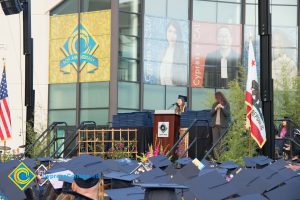 A student in regalia speaks onstage at commencement