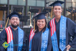 Students in graduation regalia and veteran sashes pose for photo