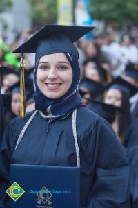 Student in headscarf and graduation regalia holds diploma