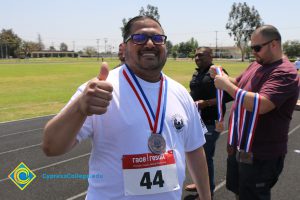 Man grinning and giving the thumb's up, wearing race number and medal