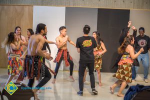 Dancers performing and getting a young man up from his seat.