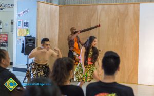 Man blowing a wind instrument while dancers perform.