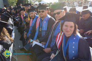 Students in graduation regalia and Veterans Resource Center sashes smile at commencement
