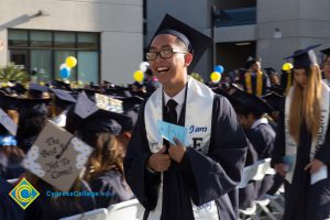 An EOPS student in graduation regalia smiles at commencement
