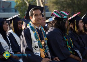 A student in graduation regalia smiles at the camera
