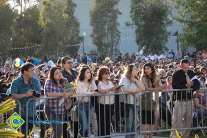 Audience members stand behind a fence at commencement