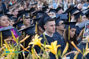 Graduates in regalia sit in the audience at commencement