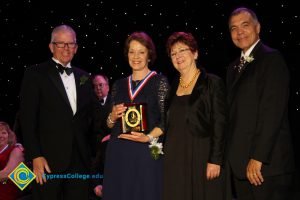 Woman in a blue dress holds and award with President Bob Simpson, a woman in a black dress and a gentleman in a black suit stand at her side smiling.