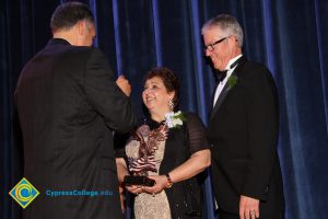 President Bob Simpson smiles as a man in a black suit speaks with a woman in a black and tan dress with an award at the 40th Annual Americana Awards.