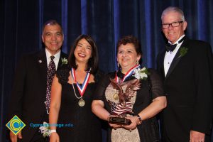 A woman in a black and tan dress holding an award, a woman in a black dress with a medal around her neck, a man in a black suit and tie and President Bob Simpson at the 40th Annual Americana Awards.