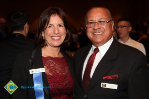 A woman in brown hair and red lace dress and black jacket with a man with glasses smiling during the 40th Annual Americana Awards.