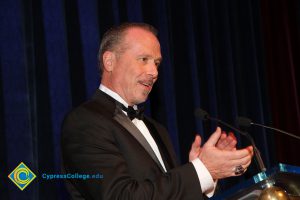 A man in a tuxedo standing at the microphone clapping during the 40th Annual Americana Awards.