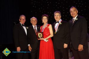 A woman in a red dress holding an award with President Bob Simpson and three other men in black suits.
