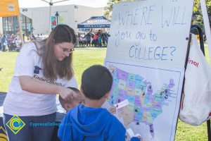 A young lady helping two little boys put a paper on a map.