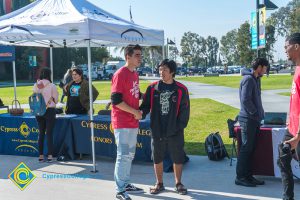 Two male students shaking hands in front of Honors Program table and canopy.