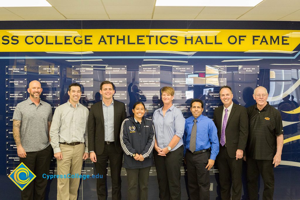 Group of men and women standing in front of Cypress College Athletics Hall of Fame wall.