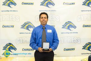 Man in a blue shirt and tie holding a medal.