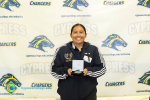 Young lady in a blue jacket with white stripes down the sleeve holding a medal.