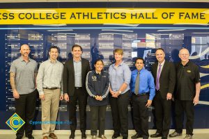 Group of men and women standing in front of Cypress College Athletics Hall of Fame wall.