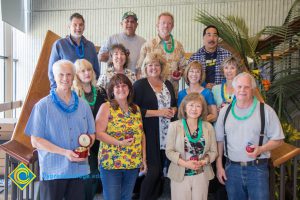 Employees wearing leis and holding ceramic apples at end-of-the-year luau