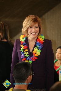 President JoAnna Schilling wearing a purple blazer and leis, smiling at employees at end-of-the-year luau
