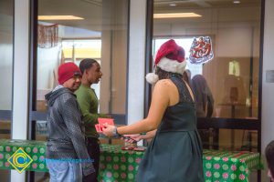 Two young men and a young lady in a Santa hat standing at a table with a green tablecloth.