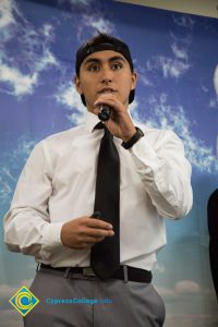 Young man in white shirt and black tie speaking into microphone.