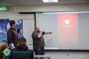 Man in a t-shirt pointing to a projection screen.